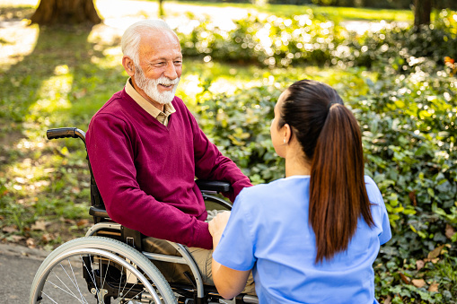 Female nursing assistant taking care of elderly man in wheelchair.