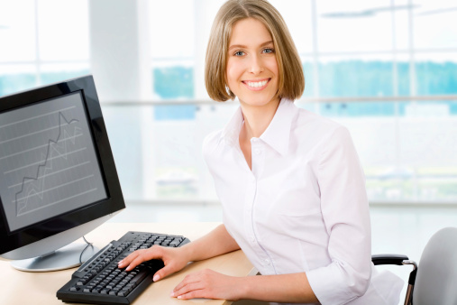 Attractive smiling young business woman using laptop at work desk