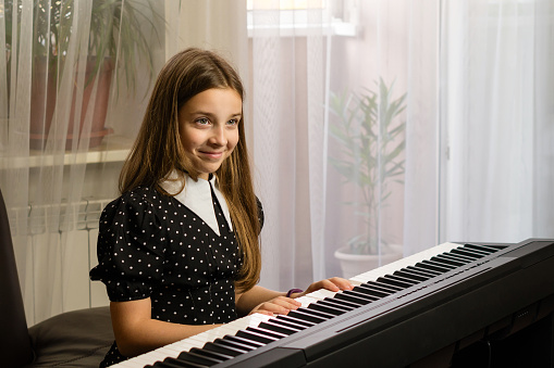 A cheerful girl practices piano at home, enjoying her music lesson in a sunny room.