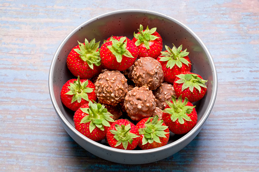 A bowl of round chocolate nut clusters with fresh strawberries surrounding the chocolate balls that are placed in the centre of the bowl