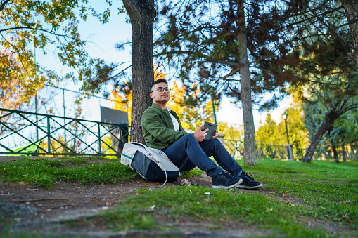 The image displays a happy student sitting on a tree branch while listening to music through his headphones.
