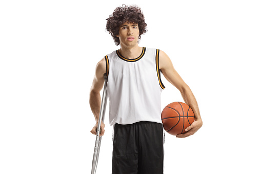 Basketball player holding a ball and leaning on a crutch isolated on white background