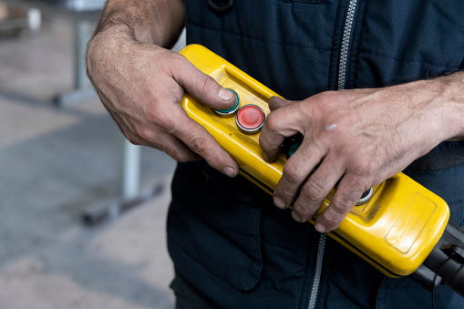 yellow overhead crane remote control held by a worker who is using it