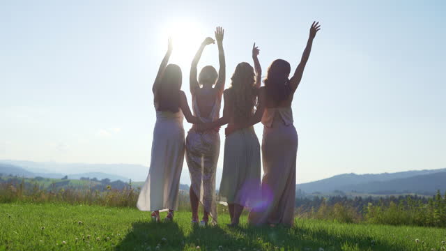 Female friends in elegant dresses looking at the mountains, embracing and swaying to the rhythm of the music
