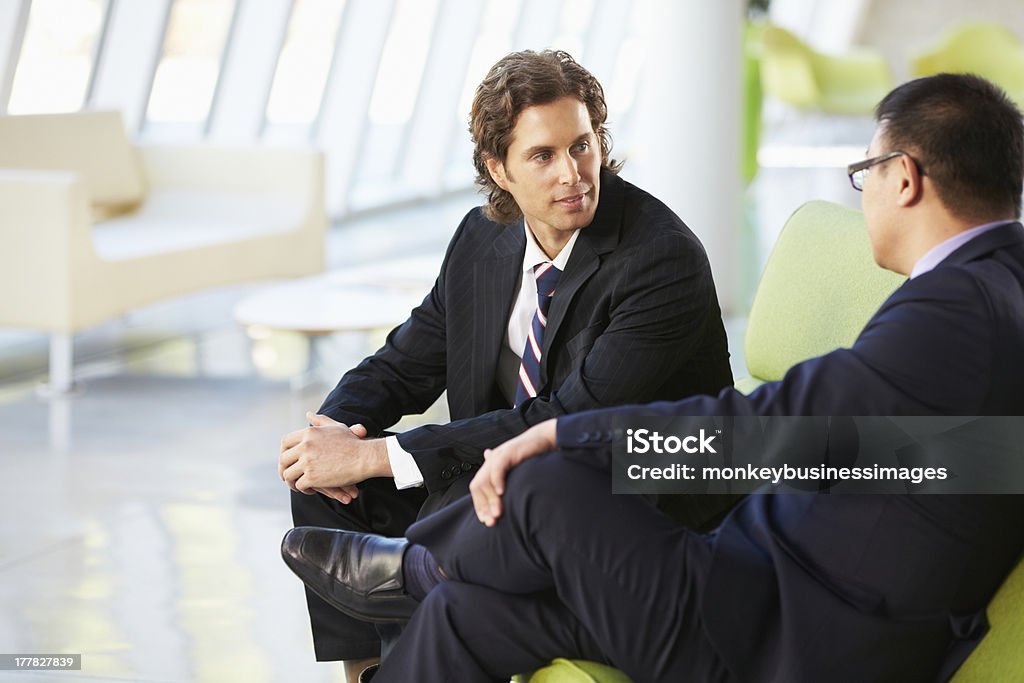 Two Businessmen Sitting On Sofa In Modern Office Two Businessmen Sitting On Sofa In Modern Office Talking 20-29 Years Stock Photo