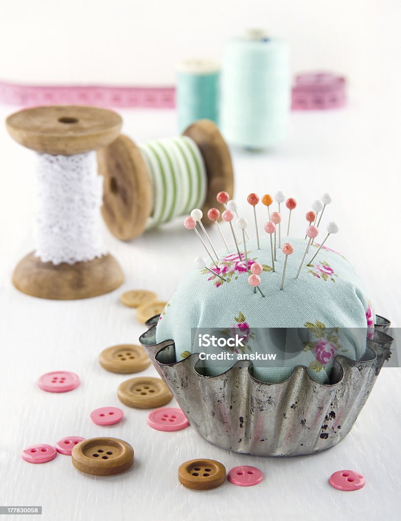 Floral pincushion in an old metal cupcake Green handmade floral pincushion in an old metal cupcake with buttons and spools of thread and lace, sewing concept background Pin Cushion Stock Photo