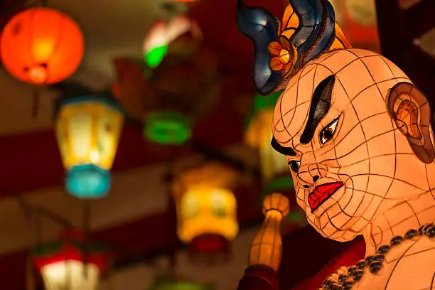 "Multicolored Asian lamps glowing, focus on foreground human shaped lantern."