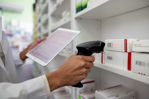 Close-up on a pharmacist taking inventory at the drugstore using a bar code reader