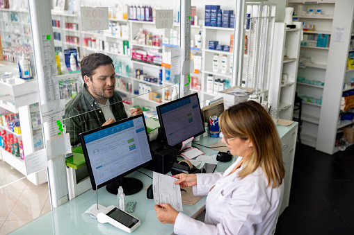 Latin American man buying medicines at the drugstore and giving the prescription to the pharmacist while waiting at the counter - healthcare and medicine concepts