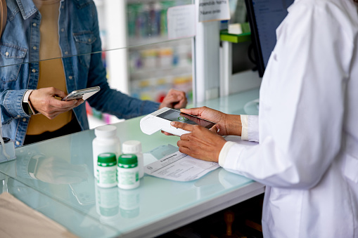 Close-up on a woman making a mobile payment while shopping for medicines at the pharmacy - tap to pay concepts