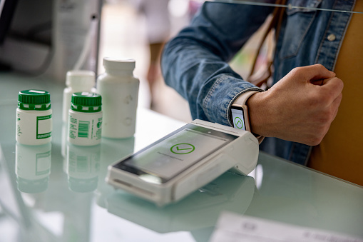 Close-up on a woman making a contactless payment at the pharmacy using her smartwatch - financial technology concepts