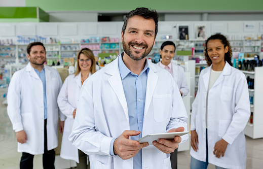 Portrait of a happy pharmacist leading a group of workers at the drugstore and smiling at the camera - healthcare and medicine concepts