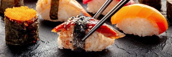 Sushi with chopsticks panorama. Unagi sushi, nigiri with eel, and other sushi and rolls, on a black background. Japanese restaurant