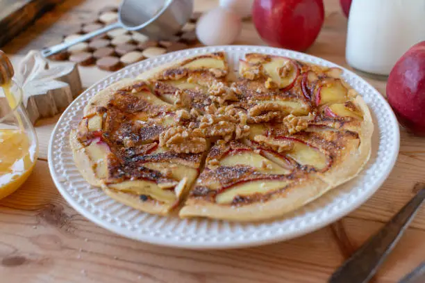 Delicious homemade apple cinnamon pancake with caramelized apples and walnuts on a plate. Closeup