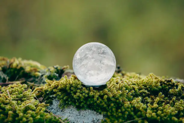 Gemstone sphere or crystal balls known as crystallum orbis and orbuculum which is the beacon of peace and harmony in environment. Natural clear quartz ball on stand on stone with moss with copy space.