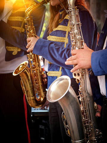 A brass band is playing in the city park. Vertical close-up images of a group of saxophonists in the foreground.