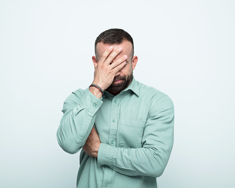 Worried mid adult men wearing green shirt covering face with hand. Studio shot, white background.