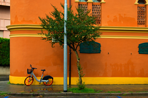 Rental bike is parked on orange background wall in Pisa, Italy. Concept of healthy lifestyle. Colorful city bike for rent. Autumn rainy weather.