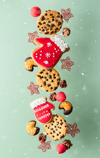 Mitten cookies with chocolate chips, marshmallows and stars fly among the snow, Christmas levitation, hovering sweets on an olive background, Merry Christmas and a Happy New Year