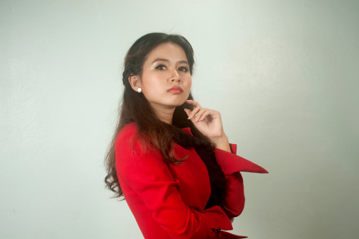 A portrait of beautiful young Asian businesswoman in red suit thinking on background.