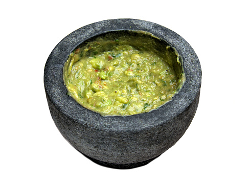 fresh guacamole in molcajete bowl (traditional mexican mortar and pestle for grinding spices and making sauces) spicy avocado dip isolated on white background, cut out (stone serveware, tableware)