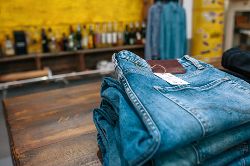 Blue jeans pants stacks over counter on vintage clothes shop with left copy space. Organized clothes ready to sell on store with industrial style. Apparel small business concept.
