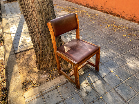 High angle view of wooden chair abandoned in the street next to tree in the city of Valencia, Spain