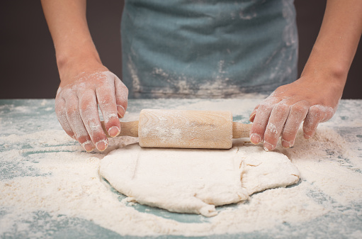 Baker rolls out dough for pizza, flatbread or pastry with rolling pin, prepare ingredients for food, baking for holidays