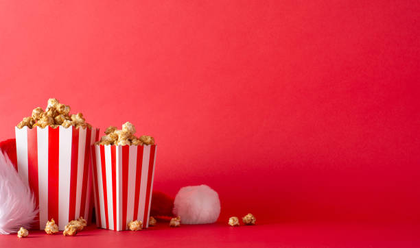 istock New Year film atmosphere: Side view table layout featuring striped popcorn boxes and elf's hat, set against a red wall for movie promotions 1778455518