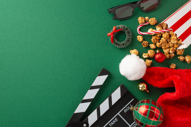 istock Seasonal cinema magic: Top view image featuring clapperboard, 3D glasses, popcorn in box, Santa's hat, balls, star decor, tiny wreath, candy corn on a green background with space for your promotion 1778455529