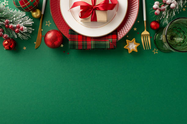 istock Festive table setting for special occasions. Top view plates, cutlery, napkin, wine glass, decorative baubles, candle, confetti, frosty fir twigs, mistletoe on green backdrop with space for text or ad 1778455966