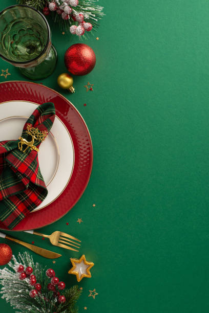 istock Inspire a festive dining experience: vertical top view of table setting with plates, golden cutlery, checkered napkin with trendy ring, wine glass, baubles, confetti, frosted fir, mistletoe on green 1778456042