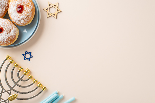 Hanukkah stylish dining presentation. Top view of traditional Jewish meal - sufganiyot, Star of David, menorah, candles on pastel beige backdrop with space for text or advert