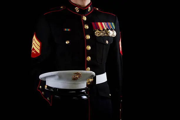 A U.S. Marine stands in the dress blue service uniform while holding his cover.