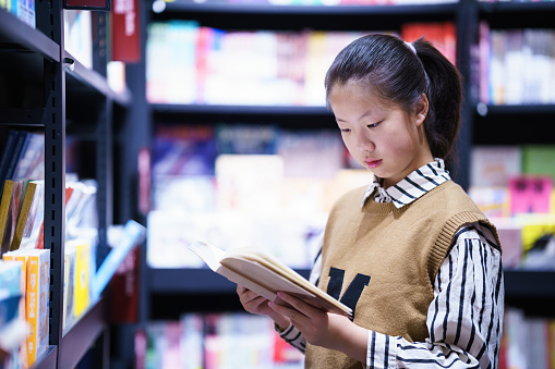Asian teenage girl reading book in bookstore at night