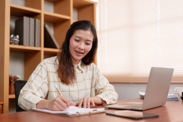 istock Asian woman, office worker writing work on sheet paper, for taking notes, before turning on laptop computer on my desk find out more, do some detailed writing, woman lowered her head wrote again. 1778482561