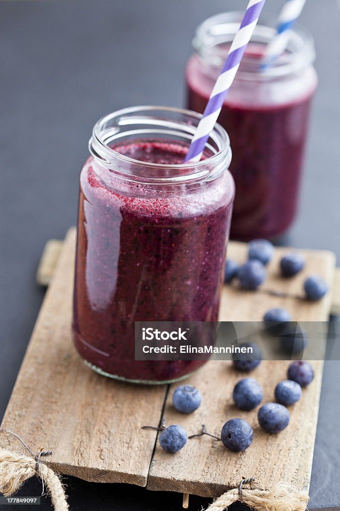 Blueberry smoothies Closeup of blueberry smoothies in glasses with striped straws on wooden serving tray with blueberries Blueberry Stock Photo