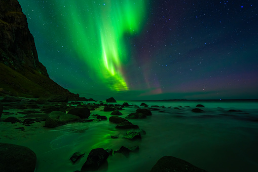 Northern lights over the beach, reflection in the silky water. Lofoten islands, Norway.