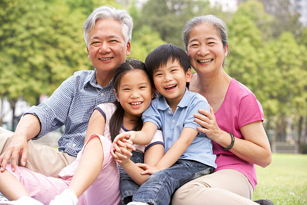 Chinese Grandparents Sitting With Grandchildren In Park Chinese Grandparents Sitting With Grandchildren In Park Looking At Camera Smiling china chinese ethnicity smiling grandparent stock pictures, royalty-free photos & images