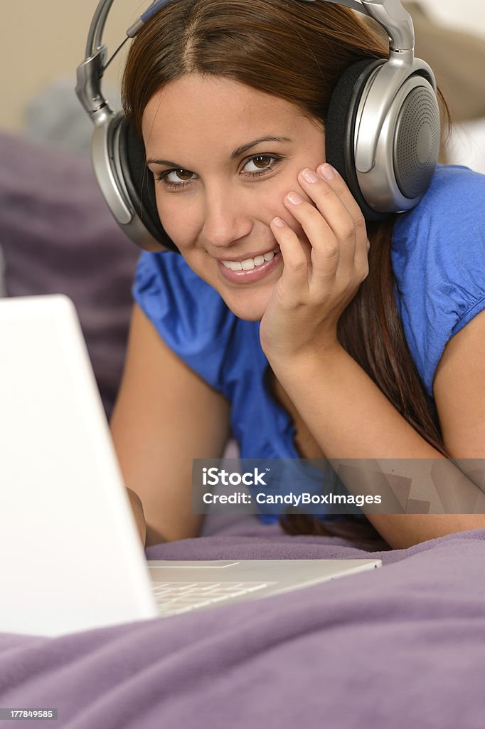 Chica joven sonriente con ordenador portátil y auriculares integrados - Foto de stock de Acostado libre de derechos