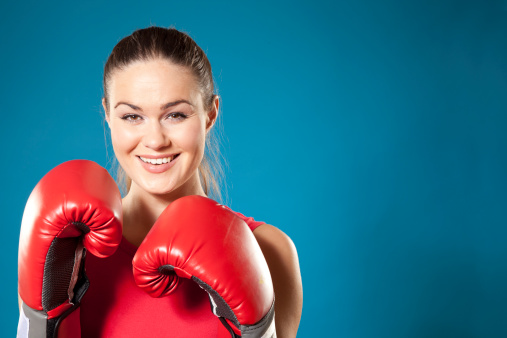 Portrait of a happy young woman wearing boxing gloves, isolated on colored background