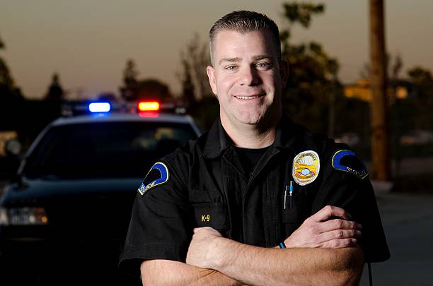 smiling officer A police K9 officer in BDU uniform smiles with his arms crossed with his patrol car in the background. police force smiling officer stock pictures, royalty-free photos & images
