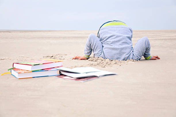 Overstrained child stucks head in sand stock photo