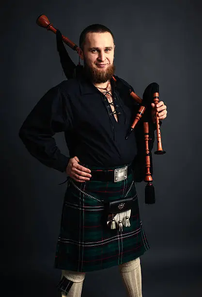 Young man with beard in scottish costume with pipe in his hand. Studio shot