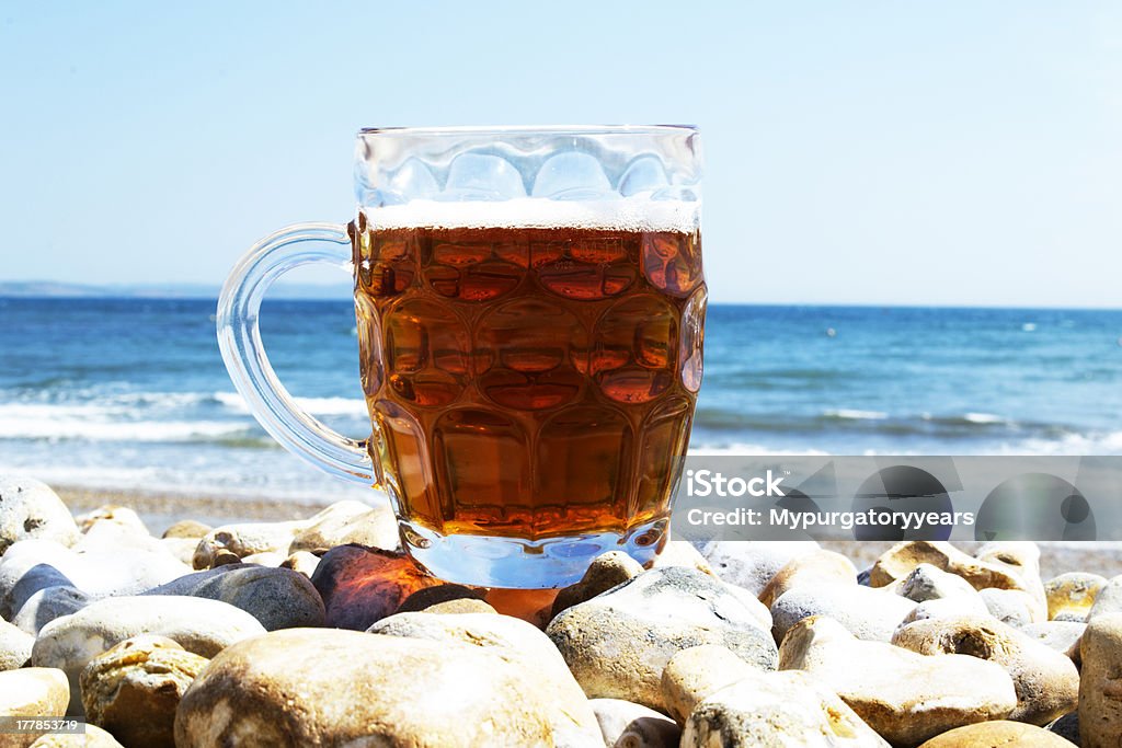 Beer on the beach A pint of ale sits on a pebbled beach with a bright blue sea backdrop. 20-24 Years Stock Photo