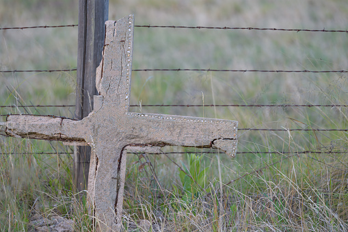 old concrete cross grave marker leaning on barbed wire fence. selective focus on the cross