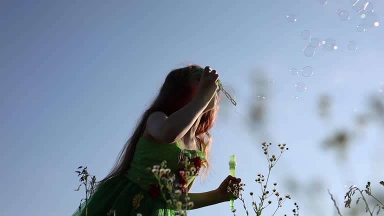 Redhead girl dressed as a fairy blowing bubbles outdoors. Cute white child celebrates St. Patrick's Day