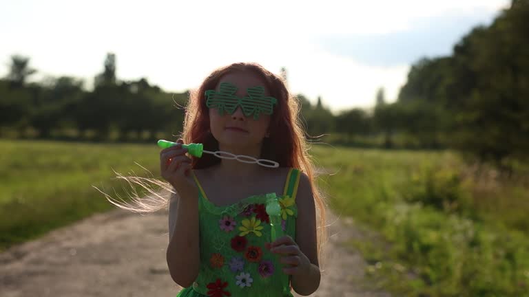 Little leprechaun girl blowing bubbles outdoors in slow motion