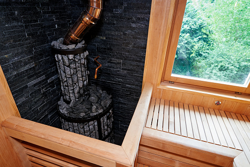 Metal stove filled with stones with a pipe in a wooden sauna. High quality photo