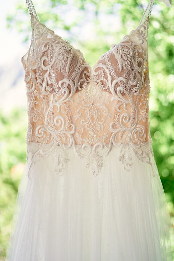 Wedding dress hanging on a hanger against the backdrop of greenery. High quality photo